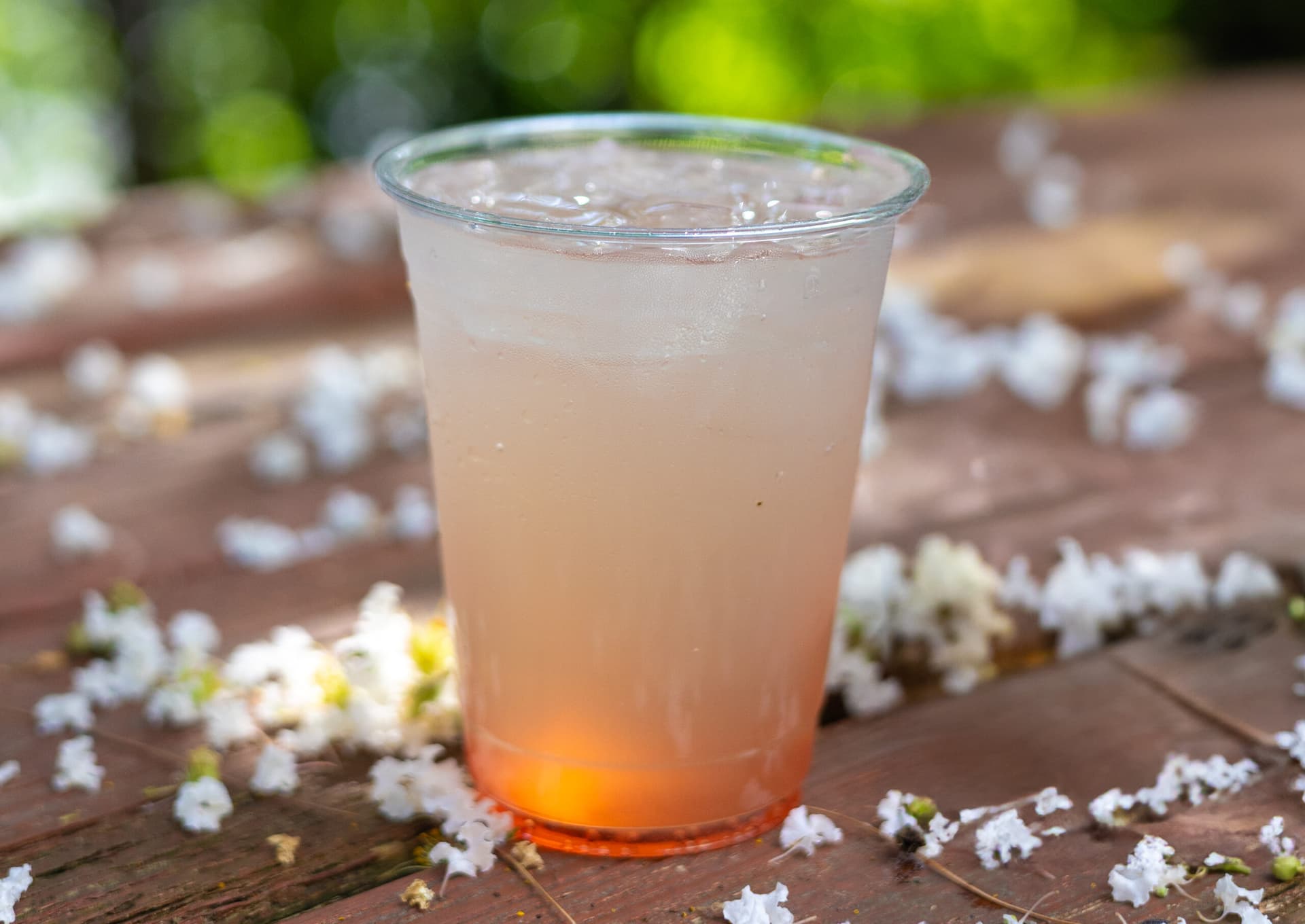 a red iced drink sitting on an outdoor table with flowers around the drink.