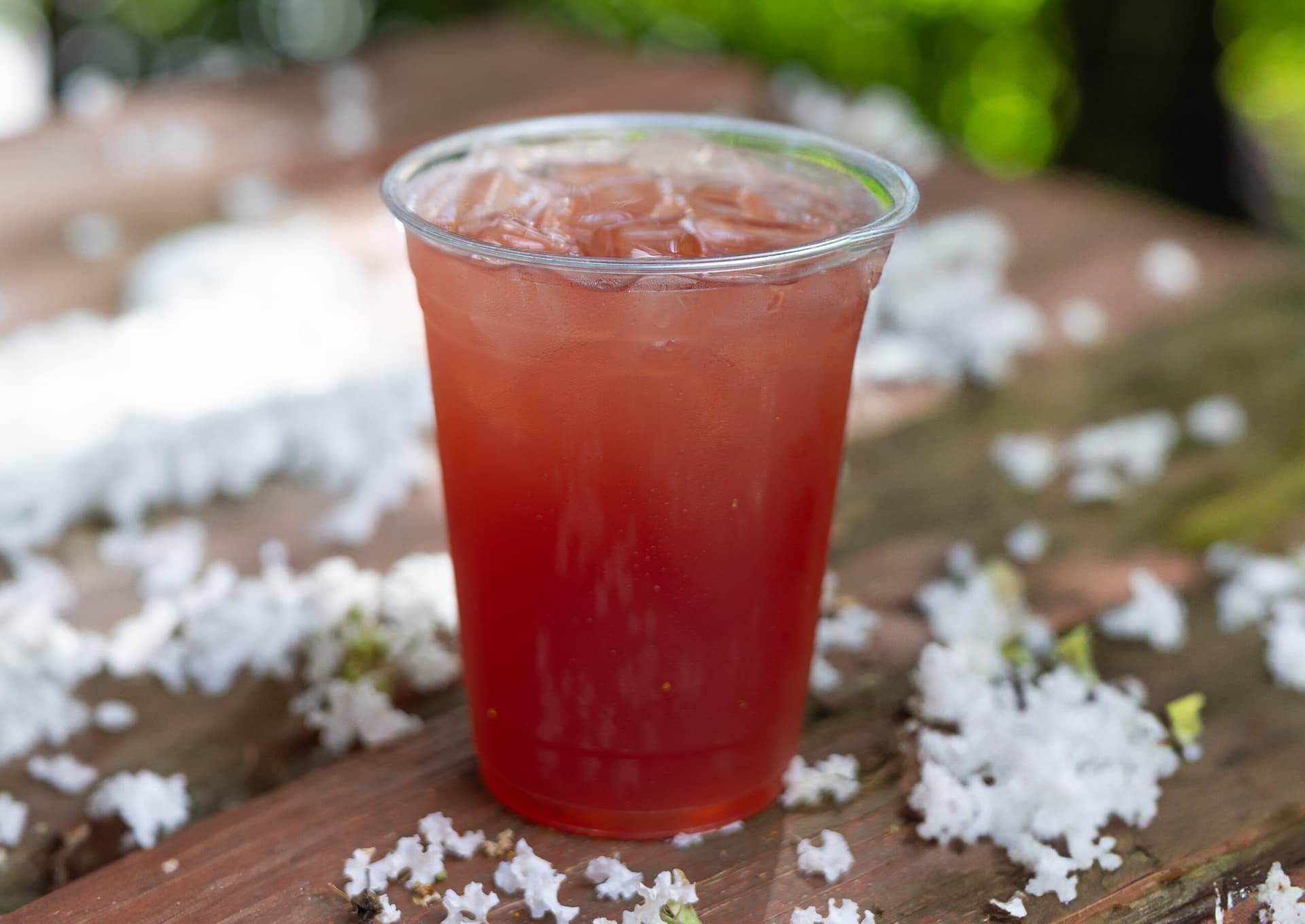 a red iced drink sitting on an outdoor table with flowers around the drink.